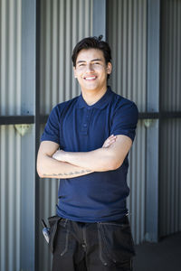 Portrait of smiling young male worker standing with arms crossed on warehouse entrance