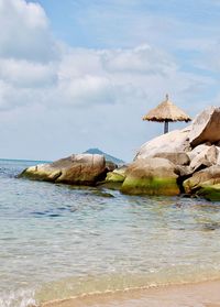 Palm frond beach umbrella on island rocky outcrop