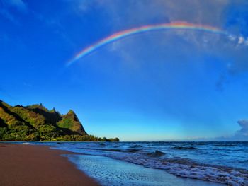 Scenic view of rainbow over sea against blue sky