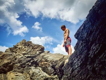 Low angle view of man standing on rock against sky