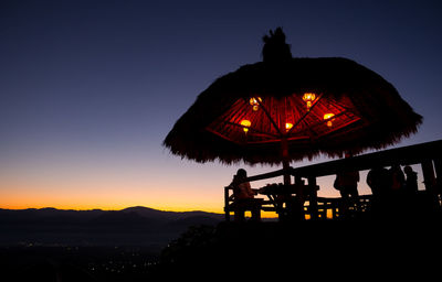 Silhouette people at illuminated temple against clear sky at sunset