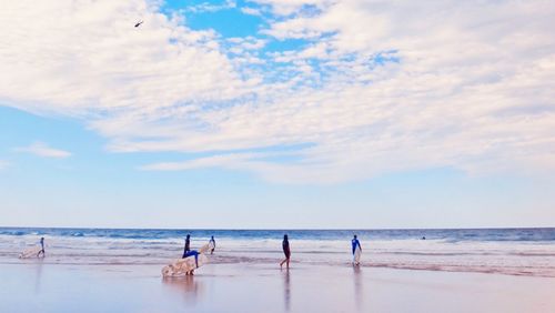 Men carrying surfboard on beach against cloudy sky