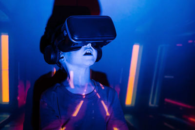 Little boy leaning on wall and exploring virtual reality under blue neon light