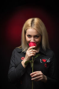Portrait of beautiful fashion model smelling rose against black background