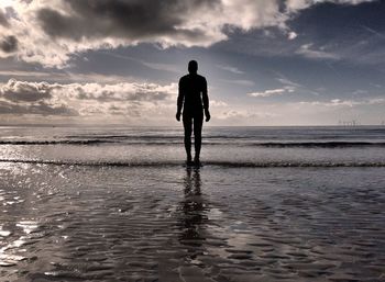 Rear view of silhouette man walking on beach against sky