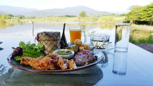 Plate of meal by glass of juice and water served on table overlooking mountains