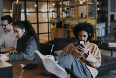 Businesswoman using smart phone by male and female colleagues working at office