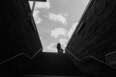 Low angle view of person on staircase amidst buildings against sky