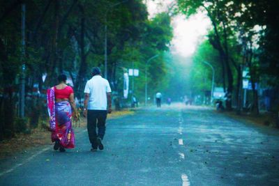 Rear view of people walking on street amidst trees