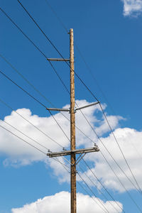 Telephone pole, electric pole against a white cloud and blue sky.