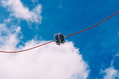 Low angle view of people enjoying suspended ride at amusement park against cloudy sky