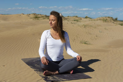 Woman with yoga mat sitting on dunes