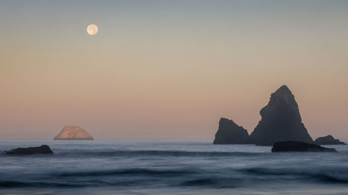 Rock formation in sea against sky during sunset