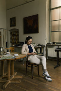 Female entrepreneur using smart phone while sitting on chair in home office