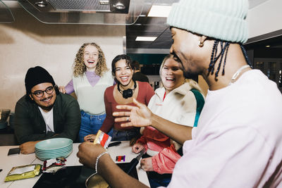 Happy multiracial young man and women looking at male friend preparing food in college dorm