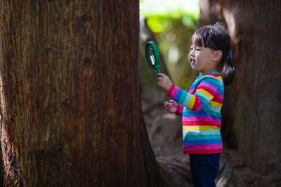 Young girl holding a magnifier and looking up in the summer forest morning