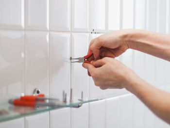 A young man pulls out a dowel from the wall using pliers.