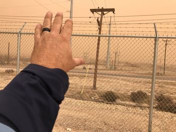 Midsection of man holding electricity pylon against sky