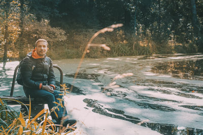 Portrait of man sitting by water during winter in forest