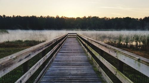 Wooden bridge over lake against sky during sunset