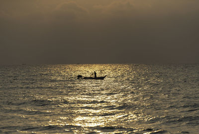 Silhouette people in sea against sky during sunset