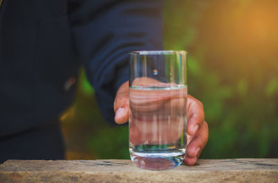 Cropped image of man holding water in glass on retaining wall