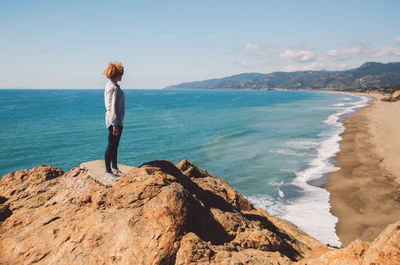 Rear view of woman standing on beach against sky