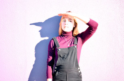 Portrait of young woman shielding eyes while standing against wall