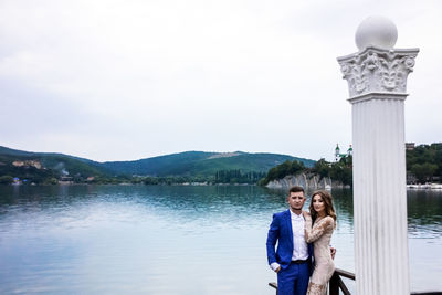 Portrait of couple standing by column against lake