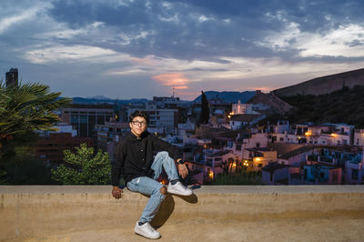 Young transgender man looking up while posing outdoors at sunset.