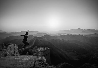 Man jumping at great wall of china against sky
