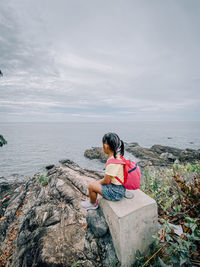 Woman sitting on rock by sea against sky