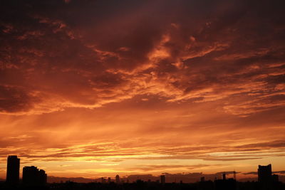 Silhouette of city against cloudy sky during sunset