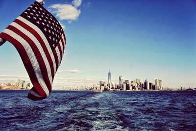 American flag waving over river with urban skyline in background