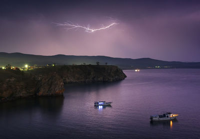 Boats sailing in sea during lightning in sky at dusk
