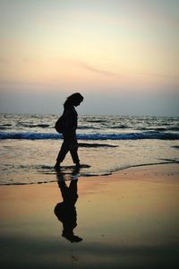 Silhouette man walking on beach against sky during sunset