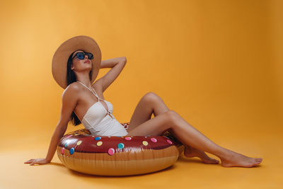 Portrait of young woman sitting against yellow background