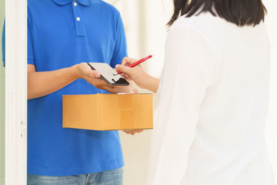 Midsection of woman signing while claiming parcel from delivery person
