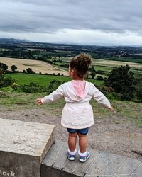 Rear view of boy standing on field against sky