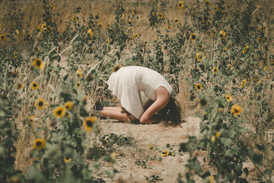 Side view of upset woman kneeling amidst plants on field