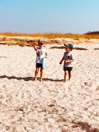 Boys standing at sandy beach against clear sky