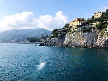 Buildings on rocks by sea against sky