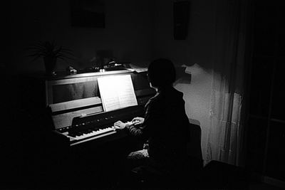 Rear view of silhouette man playing piano at home