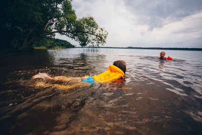 Siblings swimming in lake at forest