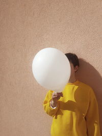 Woman covering face with balloon against wall