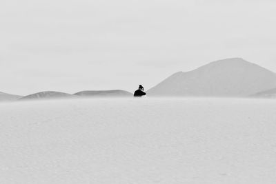 Woman sitting on sand against sky at desert