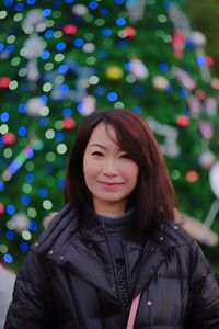 Portrait of smiling woman standing against christmas tree