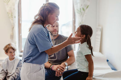 Female nurse examining throat of girl sitting with family at medical room