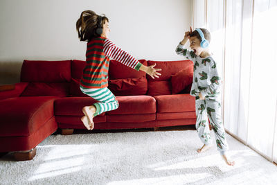 Male and female sibling wearing headphones while dancing against sofa in living room