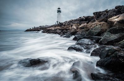 Lighthouse on rocks by sea against sky